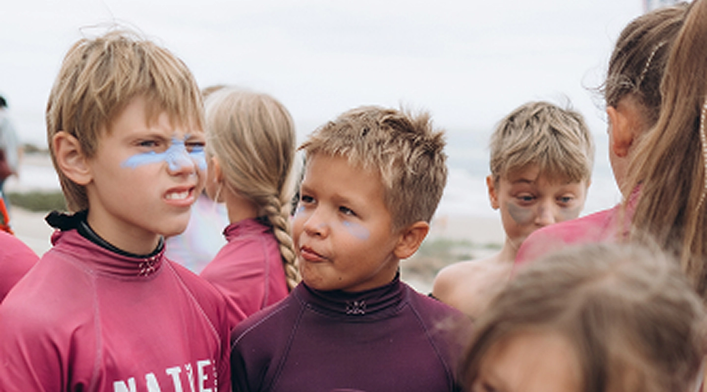 Group of children wearing rash guards and face paint standing outdoors near the beach.