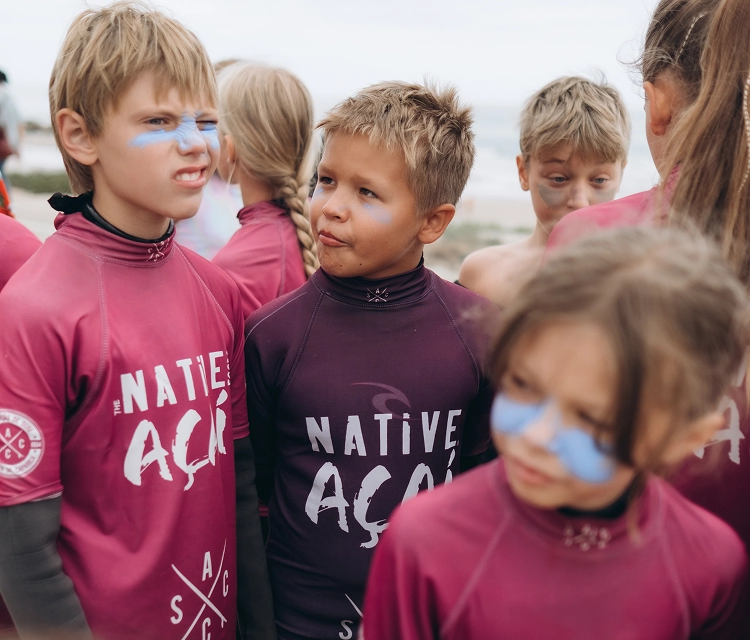 Group of children in maroon Native Açaí shirts with blue face paint standing outdoors.